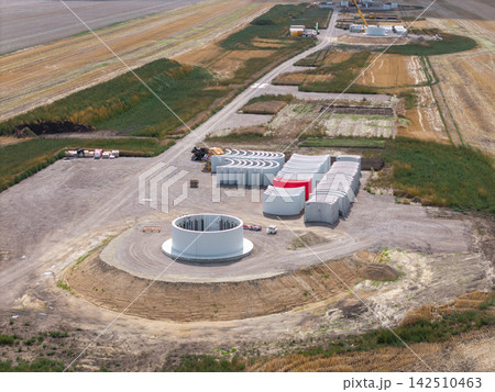 Aerial view shows circular wind turbine foundation under construction at renewable energy site. Concrete base, anchor bolts and machinery reveal engineering work for future turbine installation Aerial view shows circular wind turbine foundation under construction at renewable energy site. Concrete base, anchor bolts and machinery reveal engineering work for future turbine installation 142510463