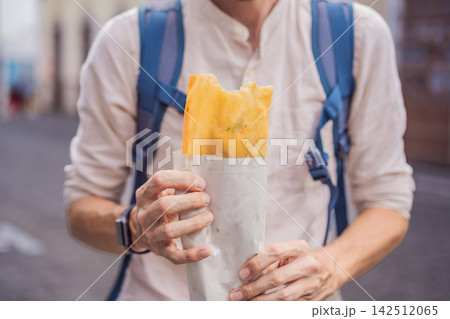 Man traveler holding a golden molote poblano traditional fried Mexican empanada outdoors on a street in Puebla Mexico with colonial city background paper wrapper local street food authentic travel. Man traveler holding a golden molote poblano traditional fried Mexican empanada outdoors on a street in Puebla Mexico with colonial city background paper wrapper local street food authentic travel. 142512065