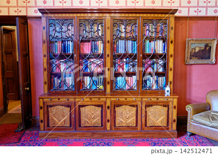 Study interior with a large wood marquetry bookcase, leather armchairs, and stenciled wallpaper borders at Knightshayes Court 142512471