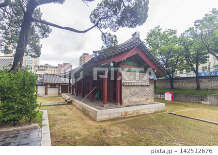 An ornate traditional Korean gate and tiled walls stand among mature trees with modern city buildings in the background. An ornate traditional Korean gate and tiled walls stand among mature trees with modern city buildings in the background. 142512676