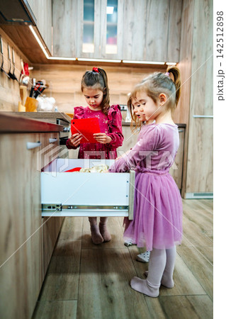 Three little girls rummaging through kitchen drawer looking for sweets Three little girls rummaging through kitchen drawer looking for sweets 142512898