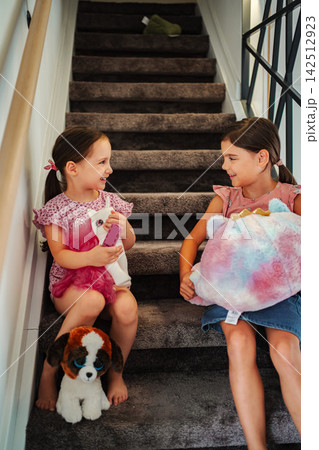 Young girls sitting on stairs playing with stuffed animals 142512923