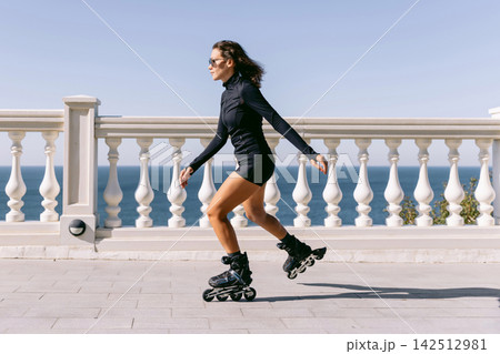 Sporty woman roller skating beside a seaside railing on a bright sunny day Sporty woman roller skating beside a seaside railing on a bright sunny day 142512981
