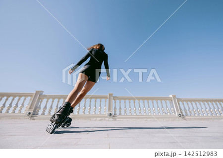 Woman roller skating under a clear blue sky during an active workout Woman roller skating under a clear blue sky during an active workout 142512983