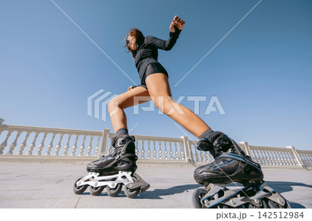 Athletic sporty woman performing a dynamic roller skating move on a sunny promenade, low angle view Athletic sporty woman performing a dynamic roller skating move on a sunny promenade, low angle view 142512984