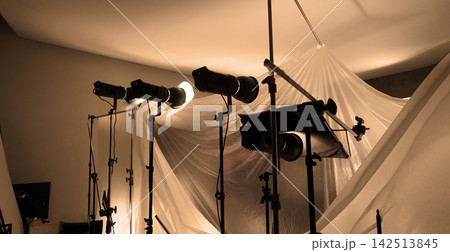 Shooting studio for photographer and creative art director with production setting up lighting flash and LED headlight on tripod and professional equipment for portrait model or product photo shoot. 142513845