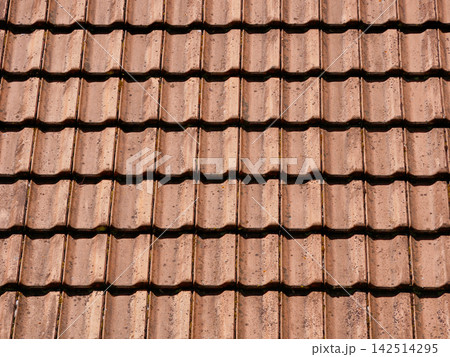 Close-up of a traditional terracotta tiled roof, showing weathered roofing materials, repeating patterns and architectural details. 142514295