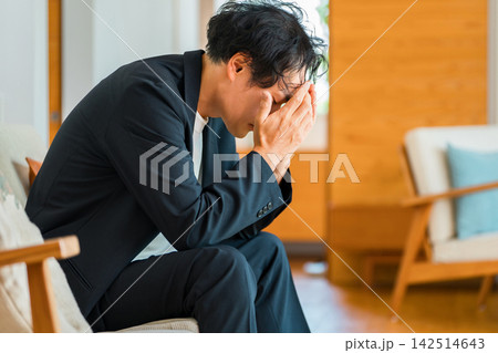 顔を覆いうつむく40代男性、仕事や人間関係に悩みストレスを抱えるイメージ 顔を覆いうつむく40代男性、仕事や人間関係に悩みストレスを抱えるイメージ 142514643