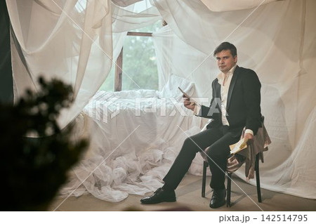 Quiet scene shows man in suit reviewing pages peacefully by window 142514795