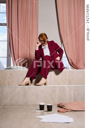 Contemplative woman in burgundy suit studying documents by window light 142514896