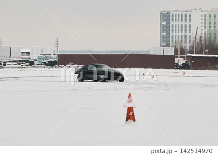 Black vehicle expertly weaving past orange markers on icy track 142514970