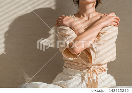肩に手を添えてセルフケアをする40代女性、光と影が印象的な美容と健康イメージ 142515236