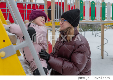 A caring adult supports a child on icy stairs, a caring caregiver helps a young girl on icy stairs outdoors, a caring adult maintains a child's balance on a slippery outdoor climbing wall. A caring adult supports a child on icy stairs, a caring caregiver helps a young girl on icy stairs outdoors, a caring adult maintains a child's balance on a slippery outdoor climbing wall. 142515629