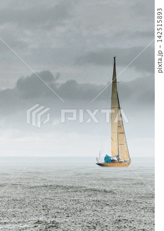vintage wooden Dragon class sailing yacht at heavy rain, sailing regatta in the Gulf of Finland, Yachtsmen are sitting amicably on board of the sailing boat, teamwork 142515893
