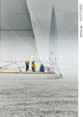 vintage wooden Dragon class sailing yacht at heavy rain, sailing regatta in the Gulf of Finland, Yachtsmen are sitting amicably on board of the sailing boat, teamwork 142515895