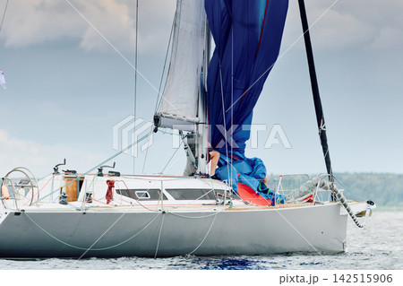 yachtsman assembles a light thin sail spinnaker during sailing regatta in the Gulf of Finland at sunny day, life jacket, board of the sailing boat, teamwork, reflections 142515906