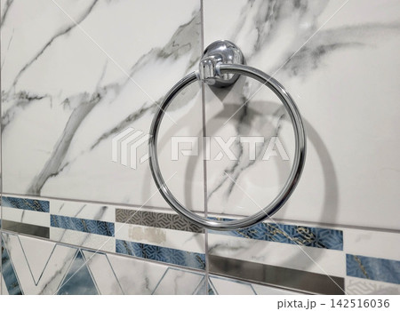 A large, smooth metal towel ring hangs on the gray-tiled bathroom wall. A large, smooth metal towel ring hangs on the gray-tiled bathroom wall. 142516036