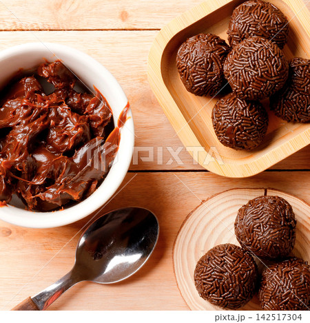 Chocolate brigadeiro with a creamy texture and chocolate sprinkle coating, presented on a bamboo tray on a wooden table. Chocolate brigadeiro with a creamy texture and chocolate sprinkle coating, presented on a bamboo tray on a wooden table. 142517304