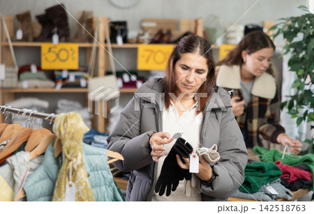 Female shopper carefully selects winter gloves in clothing store. Female shopper carefully selects winter gloves in clothing store. 142518763
