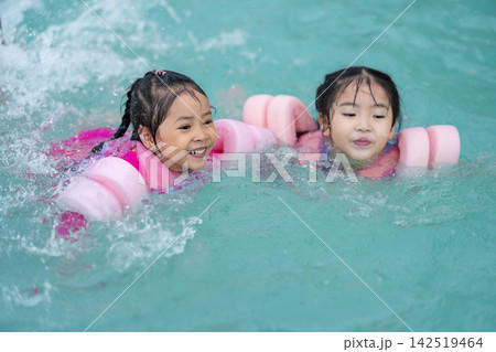 two preschool child girl playing and swimming with floaties in pool water two preschool child girl playing and swimming with floaties in pool water 142519464