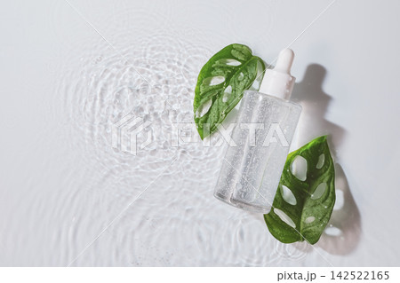 Clear skincare serum bottle and green monstera leaves floating on water with ripples Clear skincare serum bottle and green monstera leaves floating on water with ripples 142522165