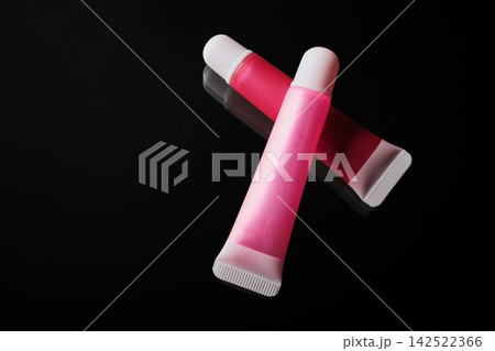 Shiny pink and red lip gloss tubes displaying cosmetic beauty products Shiny pink and red lip gloss tubes displaying cosmetic beauty products 142522366