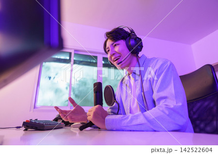 Asian male content creator talking into microphone during live stream in neon room Asian male content creator talking into microphone during live stream in neon room 142522604