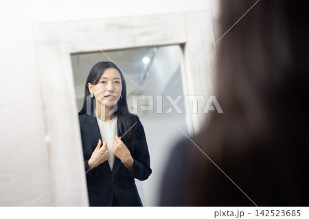 鏡の前で身だしなみを整えるスーツを着た若い日本人のビジネスウーマン 鏡の前で身だしなみを整えるスーツを着た若い日本人のビジネスウーマン 142523685