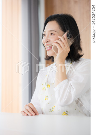 自宅でスマホを使って笑顔で電話する50代主婦のような女性、質問や問い合わせ見上げるクローズアップ 自宅でスマホを使って笑顔で電話する50代主婦のような女性、質問や問い合わせ見上げるクローズアップ 142524254