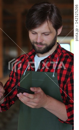 Vertical video. Male Farmer in Green Apron Tending to Goats and Using Smartphone. Vertical video. Male Farmer in Green Apron Tending to Goats and Using Smartphone. 142525266