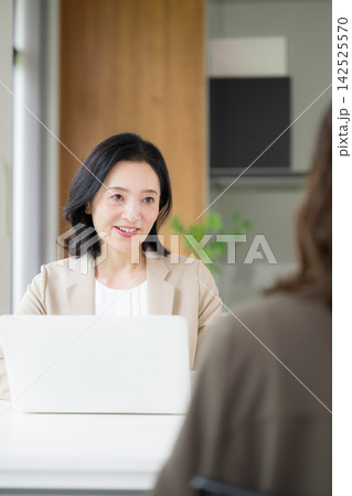 笑顔で顧客と対面相談する50代女性、オフィスで説明や提案を行うビジネスウーマン　コミュニケーション 142525570