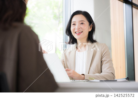 笑顔で顧客と対面相談する50代女性、オフィスで説明や提案を行うビジネスウーマン　コミュニケーション 142525572