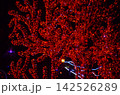 Glowing red tree branches wrapped in LED lights at night. Surreal vibrant illumination background ideal for holiday, Christmas, and night festival designs 142526289