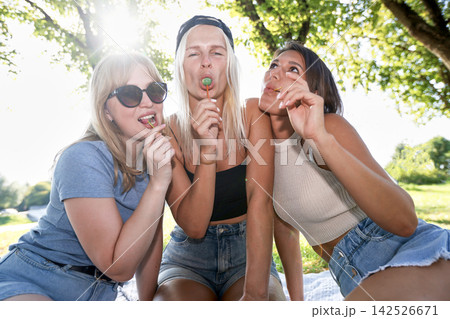 Three young female friends eating lollipops in sunny park 142526671