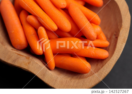 Orange baby carrots piled inside a handmade wooden bowl. Raw vegetables 142527267