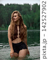 Bohemian woman with long wavy hair standing in lake with green forest background 142527902