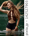 Woman in bohemian crochet top with flowing hair standing in green water 142527903