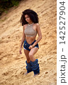 Confident young woman with curly afro hair in bohemian fashion on sandy background 142527904