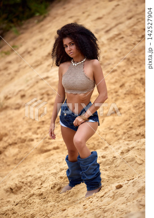 Confident young woman with curly afro hair in bohemian fashion on sandy background Confident young woman with curly afro hair in bohemian fashion on sandy background 142527904