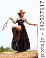 Powerful cowgirl in black dress and cowboy hat holding lasso on sandy hill 142527917