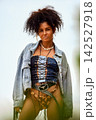 Confident young woman with curly hair in denim corset and jacket posing outdoors 142527918