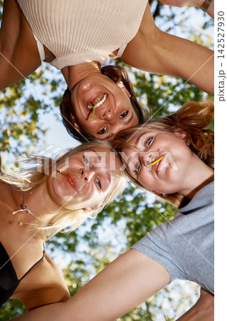 Playful young women with lollipops looking down at camera in huddle Playful young women with lollipops looking down at camera in huddle 142527930