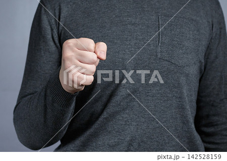 Close-Up of Man's Fist Gesture in Gray Sweater Conveying Strength and Assertive Determination Close-Up of Man's Fist Gesture in Gray Sweater Conveying Strength and Assertive Determination 142528159