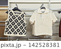 Crochet sleeveless top and cream knit polo shirt hanging on retail display rack, textured handmade fashion in neutral store interior 142528381