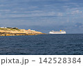 White cruise ship sailing beside rocky coastline across dark blue sea, dramatic layered clouds creating scenic maritime travel atmosphere 142528384