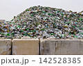 Huge pile of discarded glass bottles and broken containers behind concrete barriers at recycling facility, showing waste accumulation and material recovery 142528385