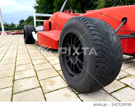 A red race car is parked on a brick surface. A red race car is parked on a brick surface. 142529598