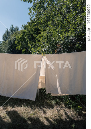 White clean laundry hanging on clothesline outdoors in sunny backyard White clean laundry hanging on clothesline outdoors in sunny backyard 142530090
