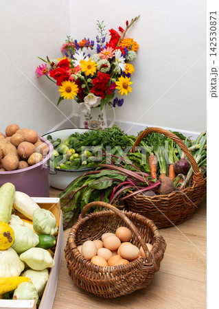 Various freshly harvested vegetables and eggs are arranged indoors. Baskets and crates hold items from the day's collection. The scene shows a mix of colors and shapes from the harvest 142530871