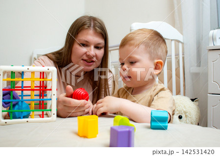 Mother and two year old son playing with colorful cubes. Parent child play teaches size order and logic. Fine motor skills development through classic toy Mother and two year old son playing with colorful cubes. Parent child play teaches size order and logic. Fine motor skills development through classic toy 142531420